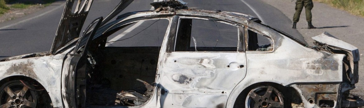 An interior ministry serviceman stands next to a burnt car in Mukacheve